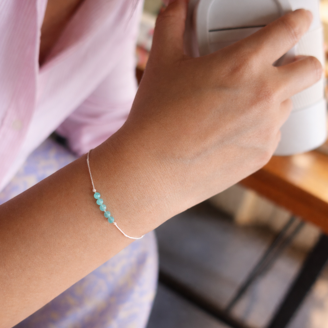 Hand wearing a turquoise beaded bracelet on a blurred indoor background