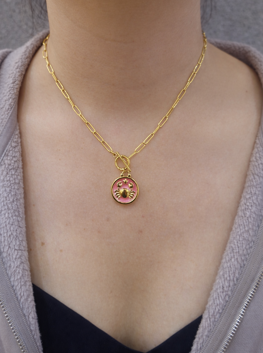 Gold plated necklace with a pink pendant on a person .