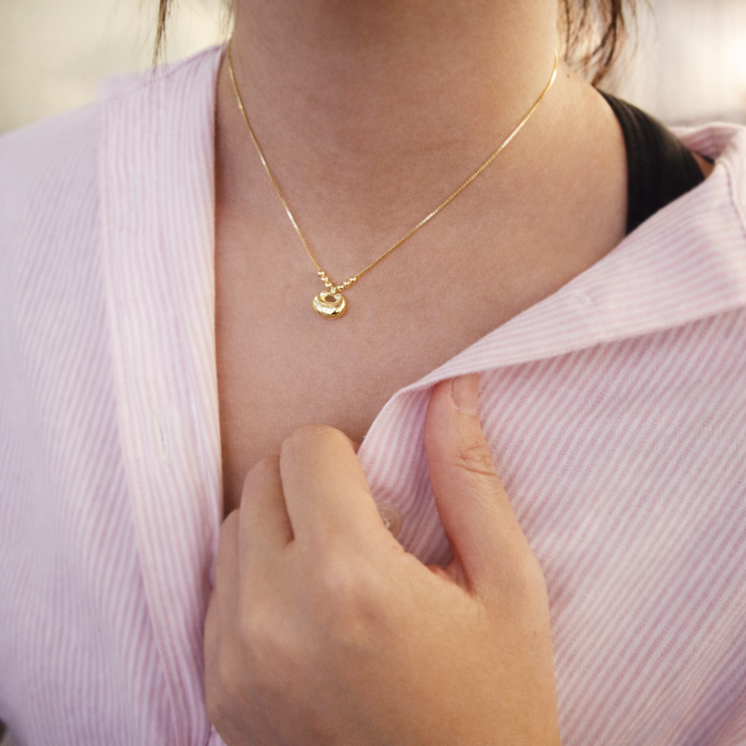 Person wearing a gold plated necklace with a pendant 