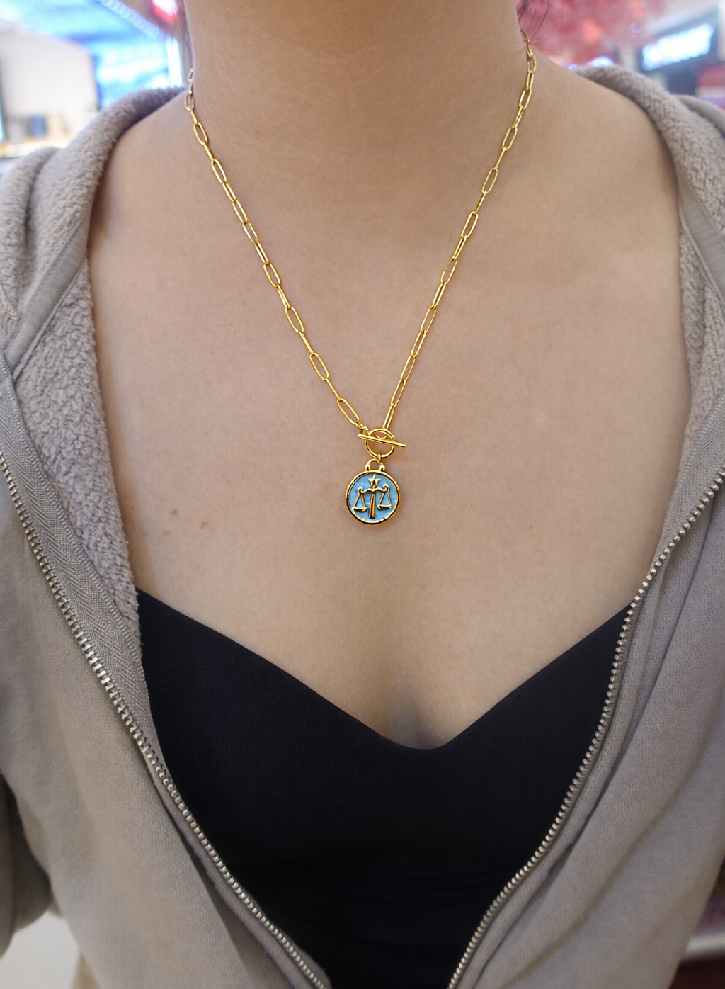 Gold plated necklace with a blue libra pendant worn by a person 
