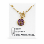 Gold necklace with a purple scorpio pendant on a white card