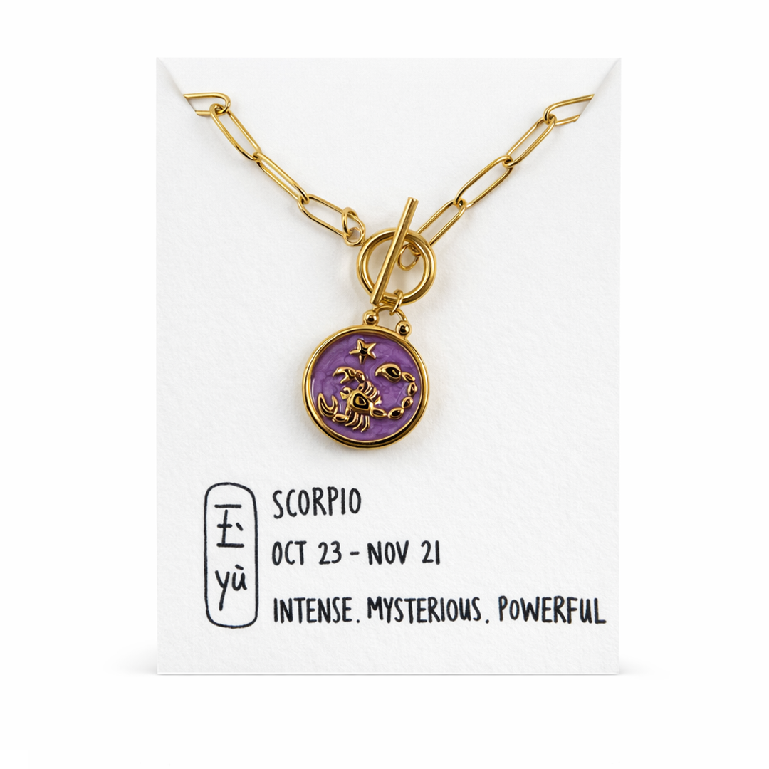 Gold necklace with a purple scorpio pendant on a white card